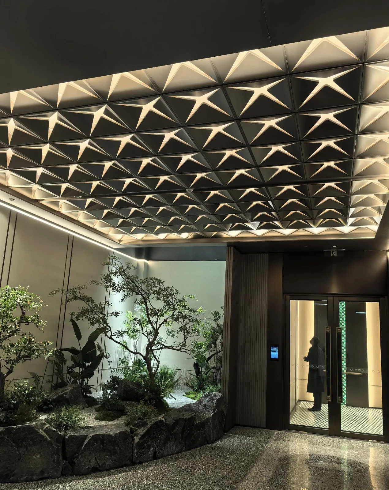 3D faceted aluminum ceiling with integrated lighting above an indoor garden