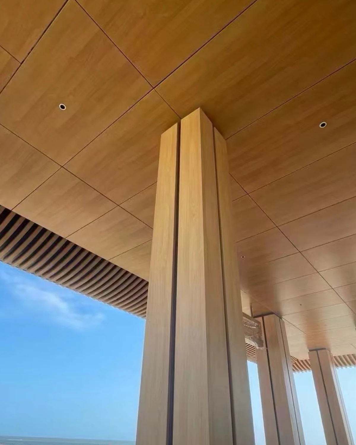 Warm-toned soffit surfaces with recessed lights meeting a tall wrapped support and narrow edge slats