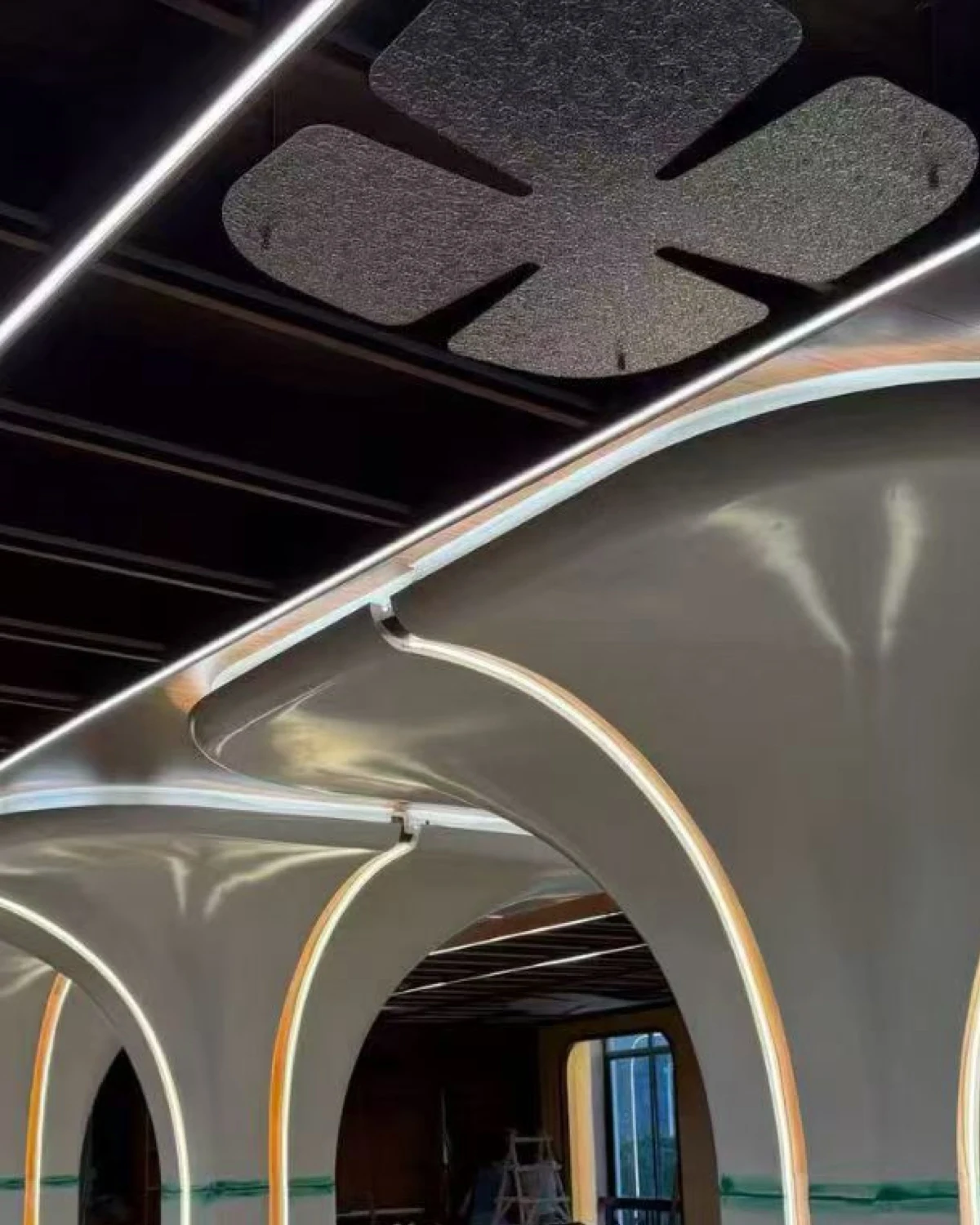 White branching column forms meeting curved ceiling surfaces beneath linear lights and a dark ceiling grid