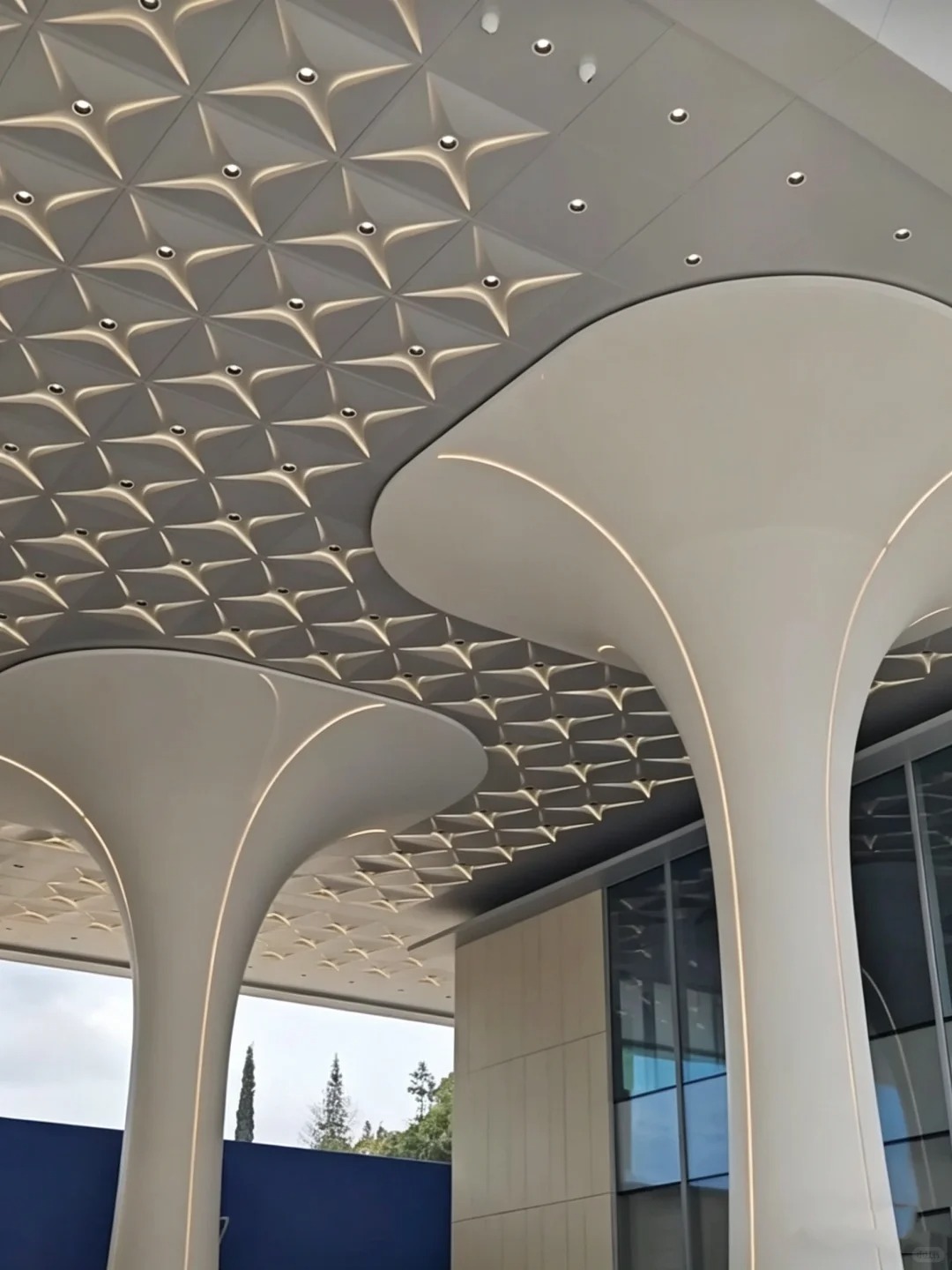 Curved solid aluminum ceiling panels with recessed downlights and patterned feature modules