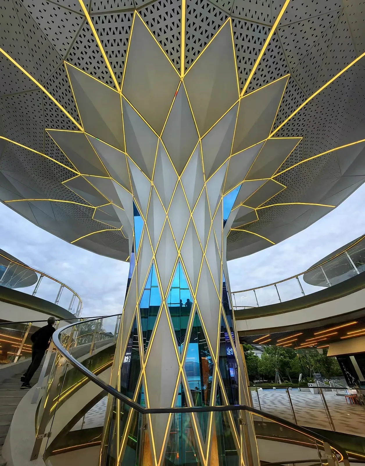 Completed tree-form folded solid aluminum elevator enclosure opening into a perforated canopy with integrated linear lighting in a Guangzhou commercial plaza.