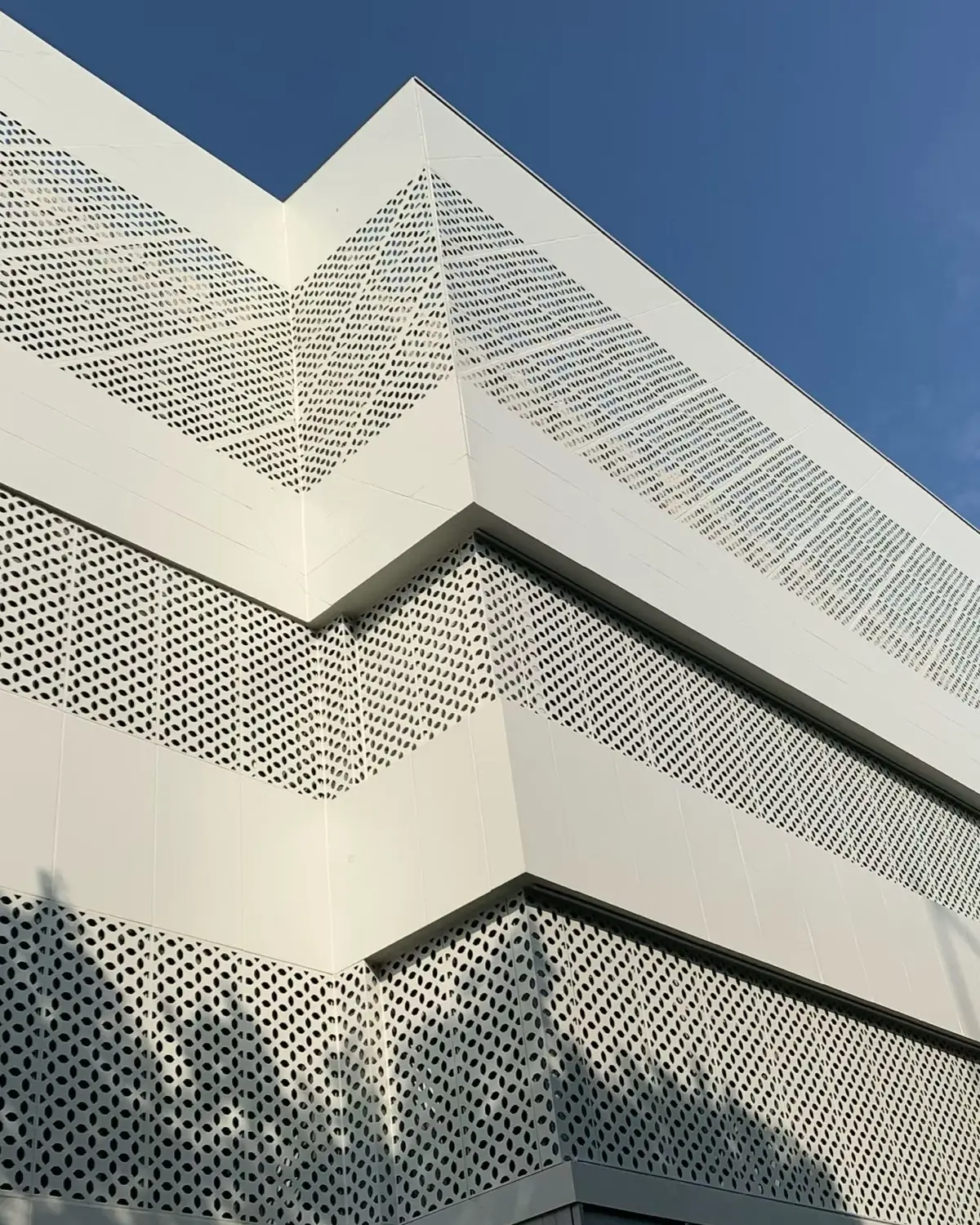 Low-angle view of a white building corner with perforated bands, unperforated areas and visible panel joints