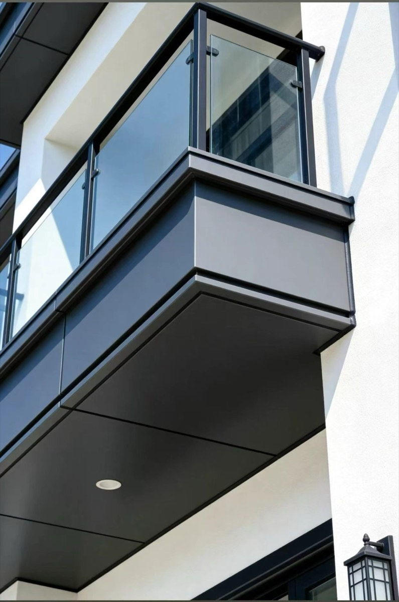 Dark balcony fascia and soffit panels meet at an outside corner below a glass balustrade, with a recessed light underneath.