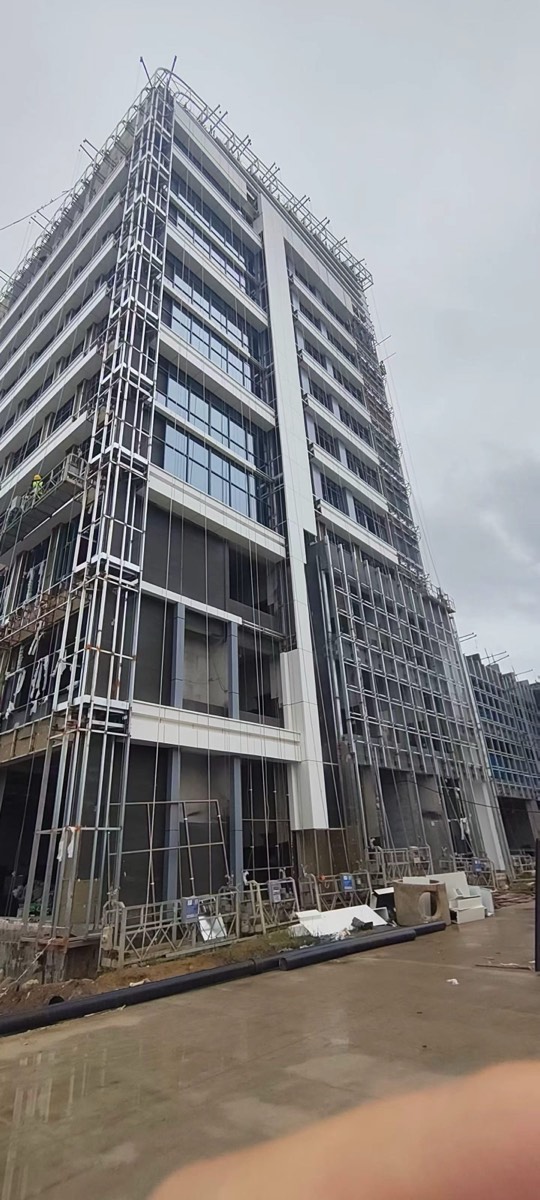 Low-angle view of a tall building corner with white bands, dark facade areas and open framing near scaffolding.