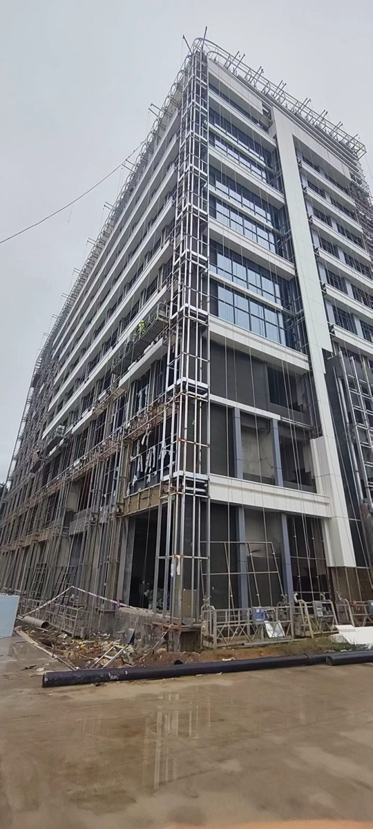 Tall building with white facade bands, dark panel zones, exposed framing and access equipment.