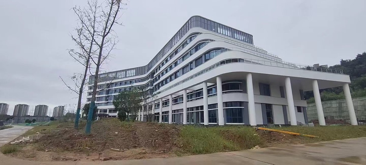 Wide site view of curved white facade bands, dark glazing and a projecting wing above round columns.