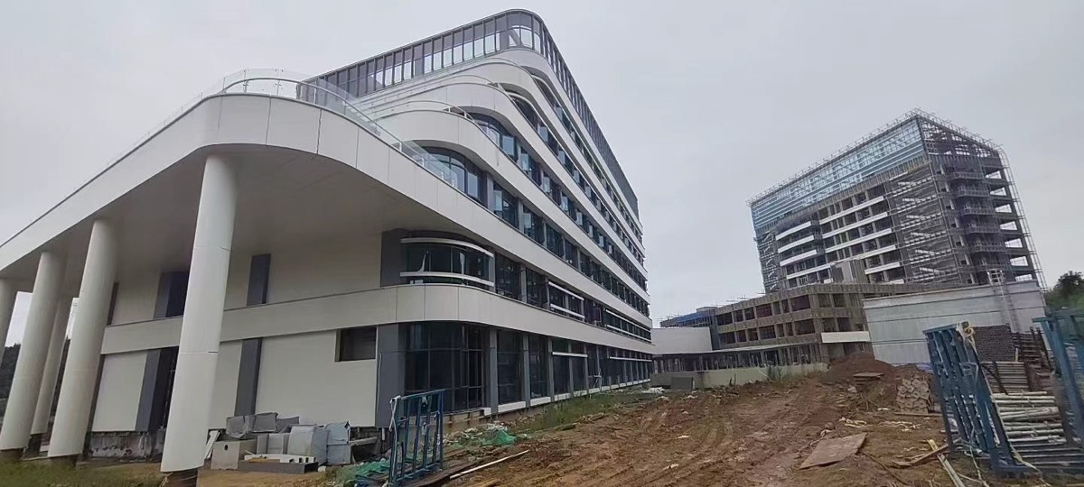 A wide projecting soffit below curved white facade bands and dark glazing, with columns and construction materials below.