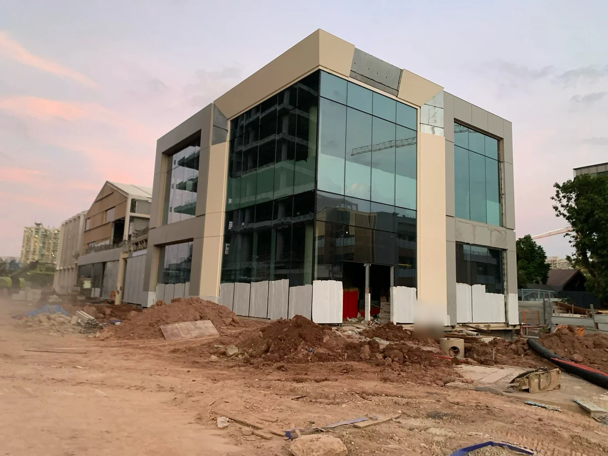 Partially installed beige solid aluminum cladding framing glazed facades at a construction site