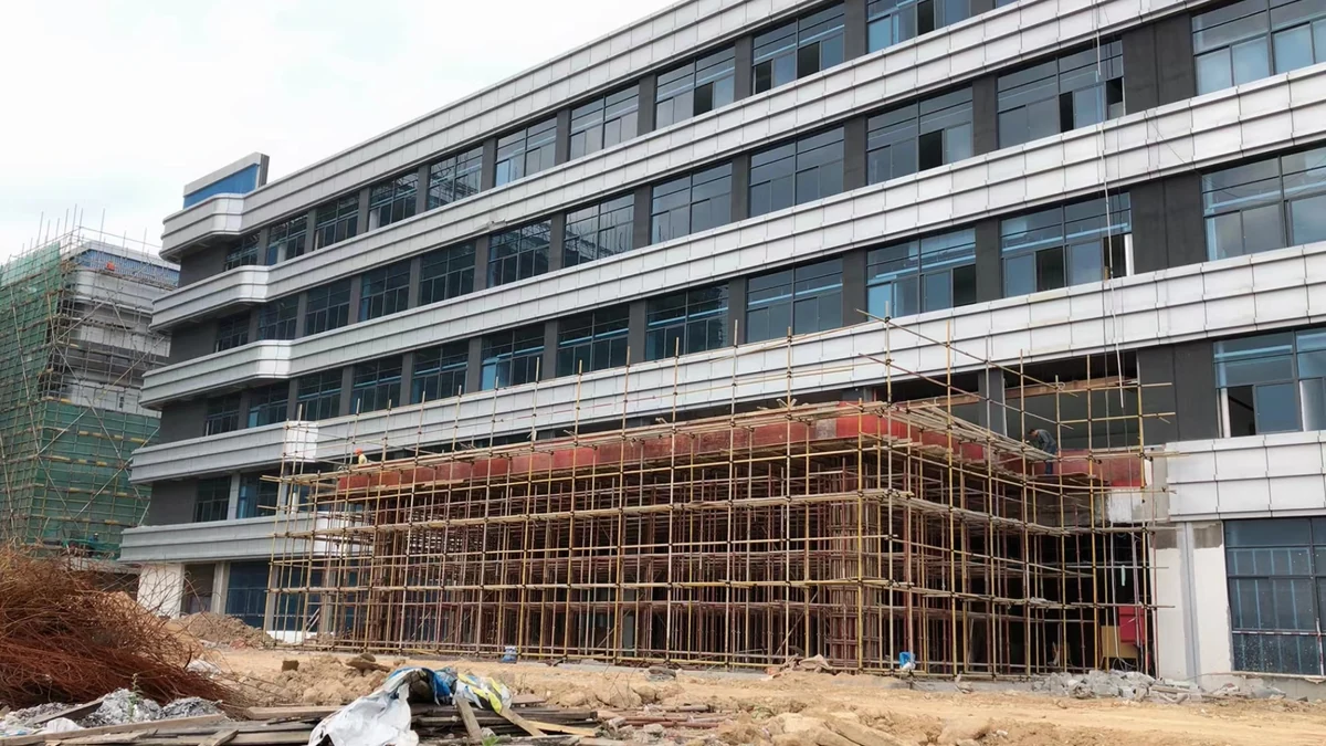 Wide construction view of white solid aluminum cladding bands across a multi-storey glazed facade